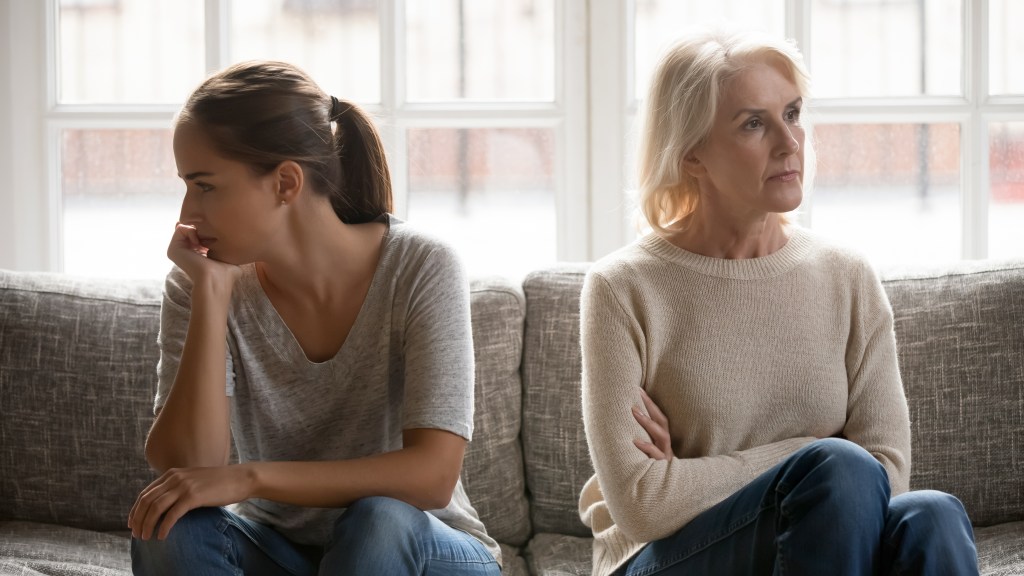 In the quarrel, the elderly mother, the grown-up daughter sit on the sofa separately, having conflicts, misunderstandings between generations.